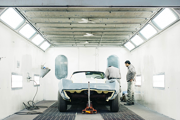 Two men working on an automobile in a paint finishing plant