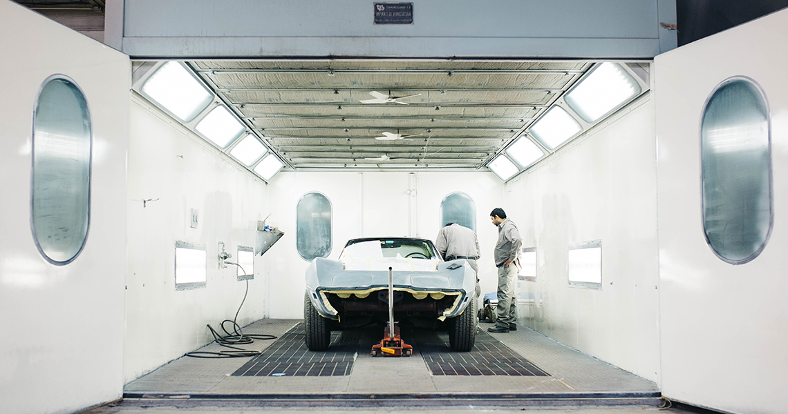Two men working on an automobile in a paint finishing plant