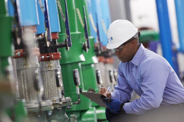 Man in a safety helmet kneeling inspecting a machine