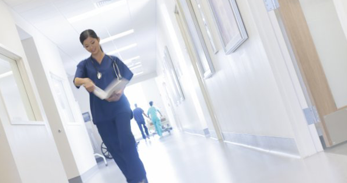 A nurse in scrubs walking down a passage in a hospital