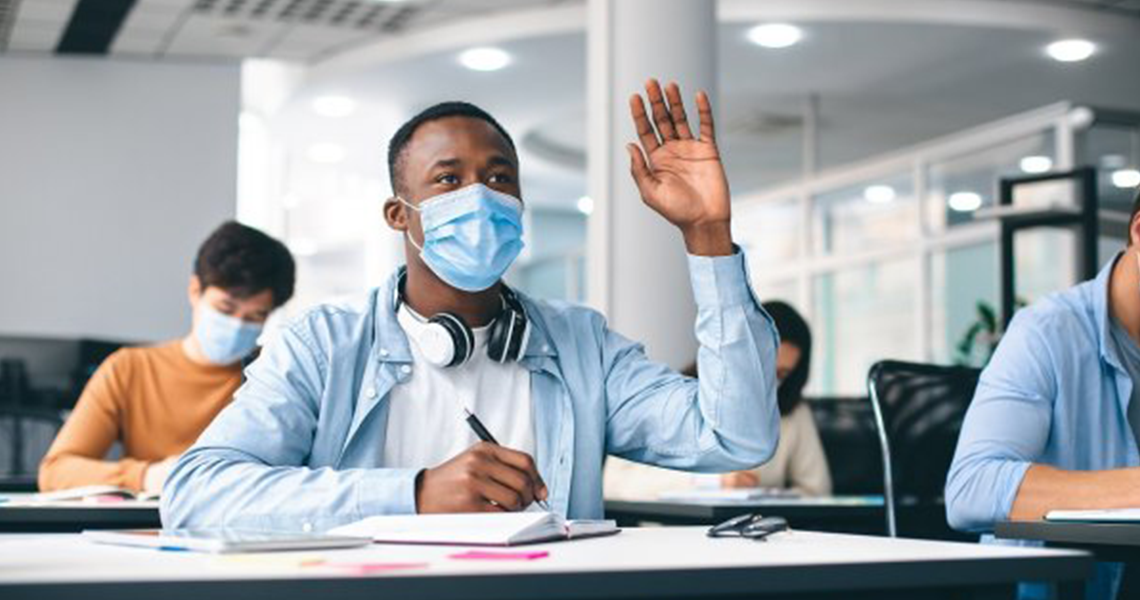 University student wearing a face-mask and raising his hand