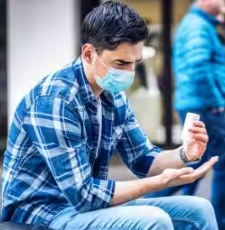 A man wearing a face-mask and applying hand sanitizer on his hands 