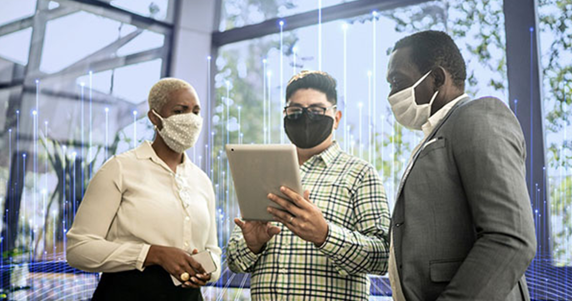 Three colleagues wearing masks looking at a tablet