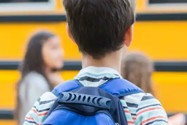 Rear view of a kid carrying a backpack in school premises