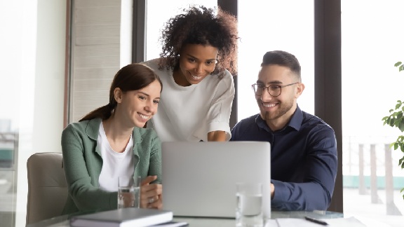 Group of employees smiling while working on a laptop in an office