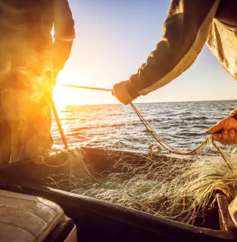 Close-up of two fishermen gathering a fishing net in a boat at sunrise