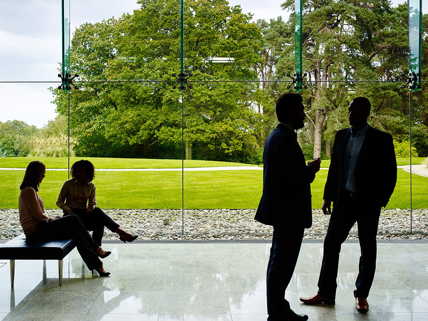 Silhouette of people in an office building with glass windows behind them